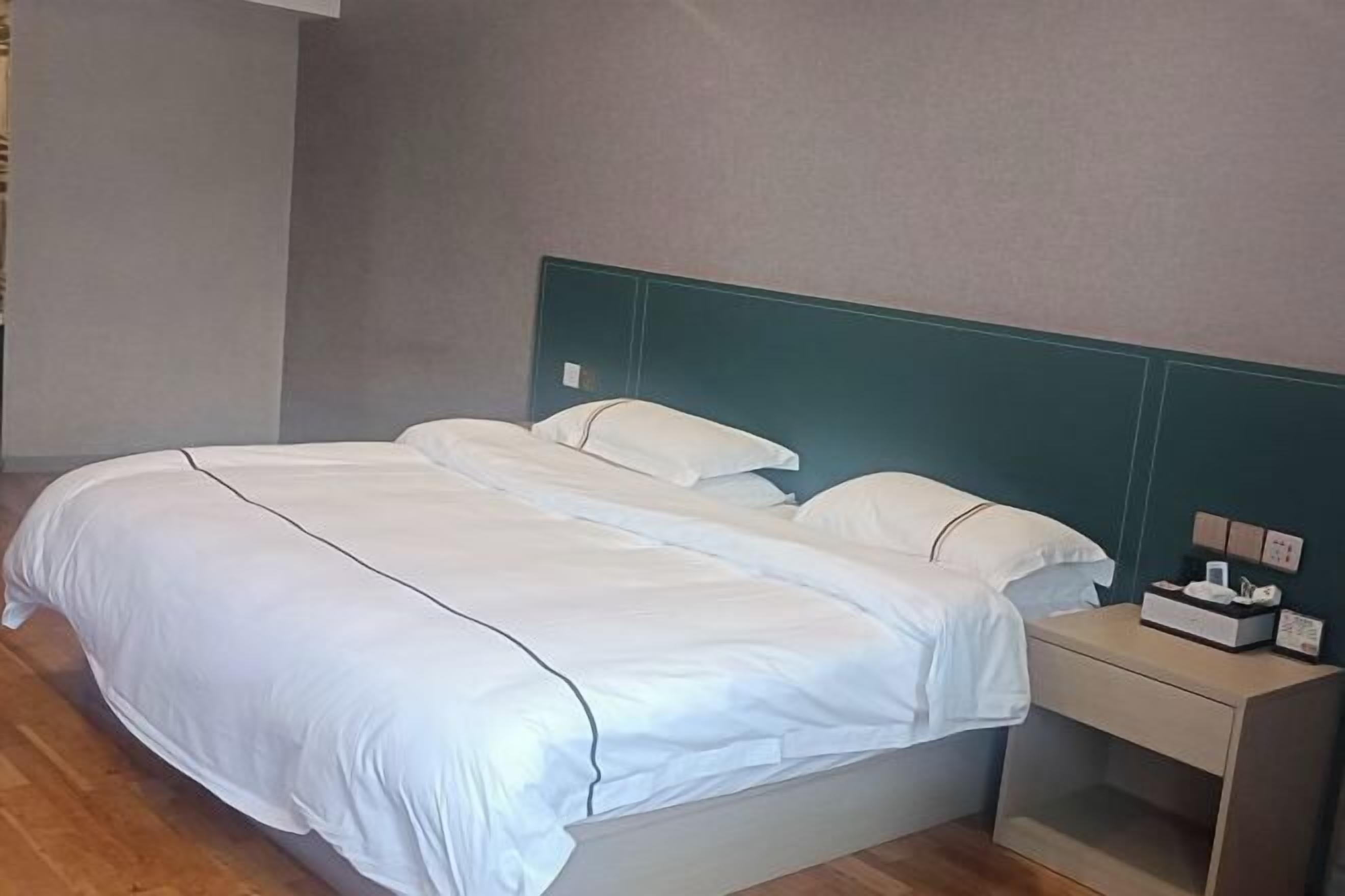 Una cama bien tendida con sábanas blancas, una mesita de noche de madera con una lámpara y un interruptor de luz en la pared.
