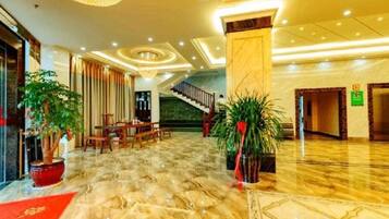A hotel lobby with a marble floor, a staircase, and potted plants.