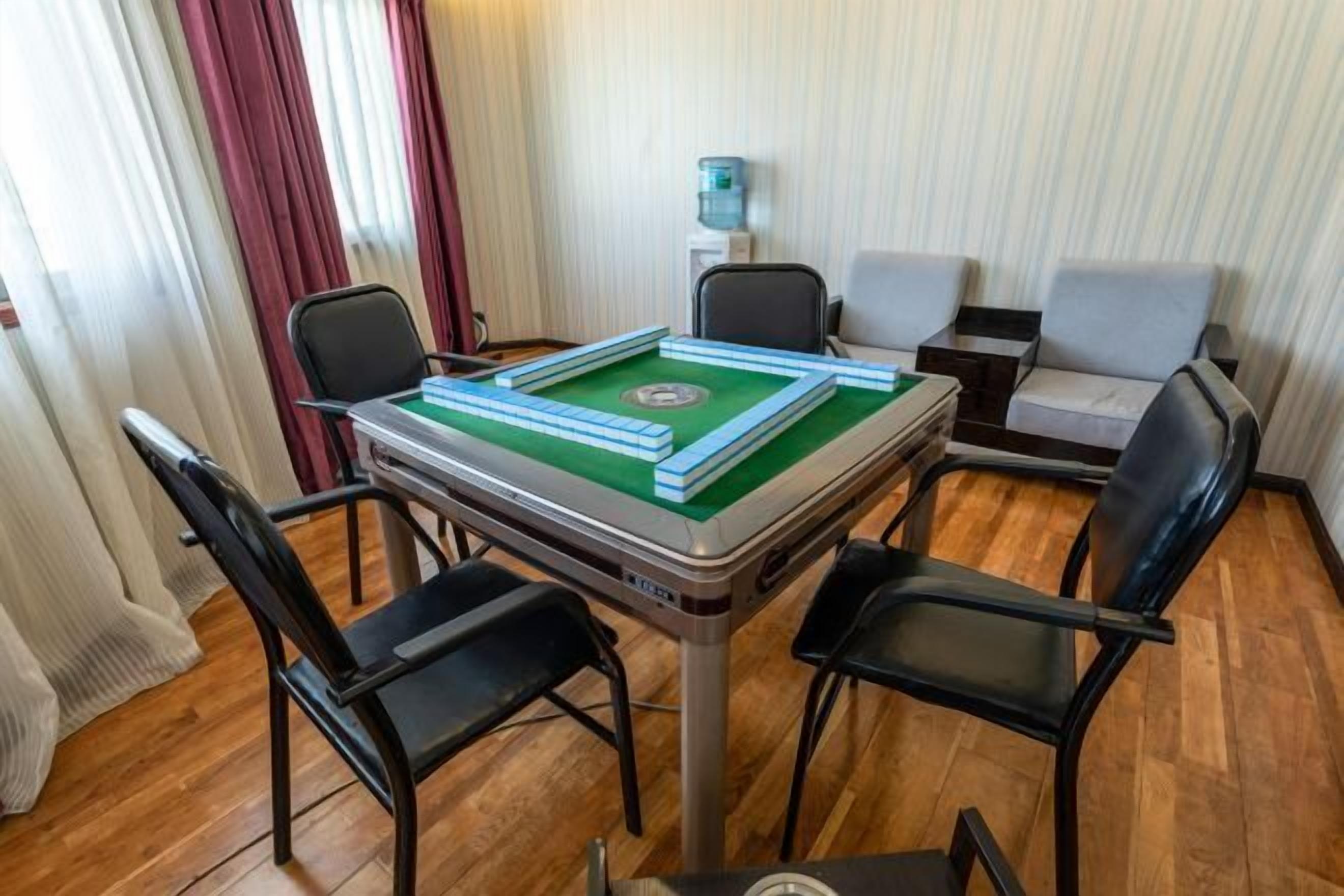 Una habitación con una mesa de billar verde, cuatro sillas negras, un sofá y un dispensador de agua.