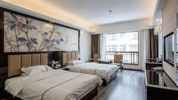 A hotel room with two beds, a TV, a desk, and a large window.