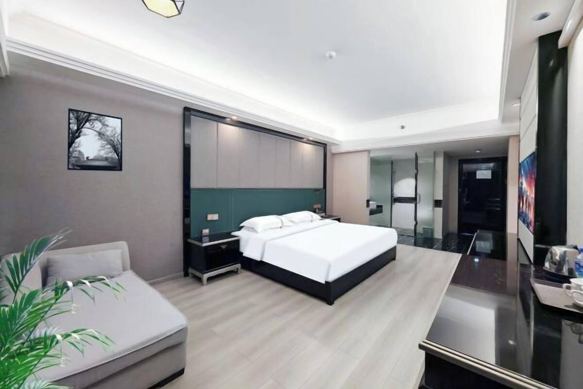 A modern hotel room with a large bed, bedside tables, a desk, and a plant.