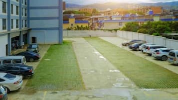 Un estacionamiento con coches, un edificio de varios pisos y una zona verde.