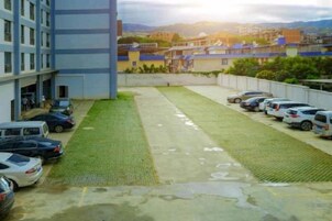 Un estacionamiento con coches, un edificio de varios pisos y una zona verde.