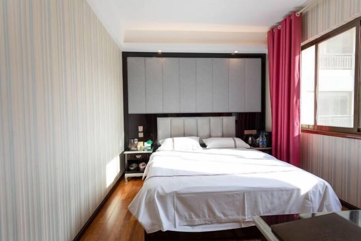 A neatly arranged hotel room with a large bed, a nightstand with a lamp, and a window with curtains.