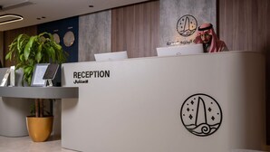 A reception desk with a sign reading "RECEPTION" and a logo with Arabic script. - Seafront Luxury Suites Jeddah Corniche (Jeddah)