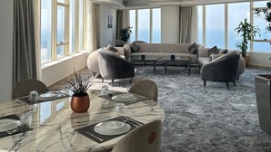 A modern dining area with a marble table, grey upholstered chairs, and a view of the city through large windows. - Seafront Luxury Suites Jeddah Corniche (Jeddah)