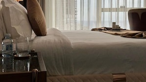 A hotel room with a bed, a bedside table with a lamp, and a view through sheer curtains. - Seafront Luxury Suites Jeddah Corniche (Jeddah)