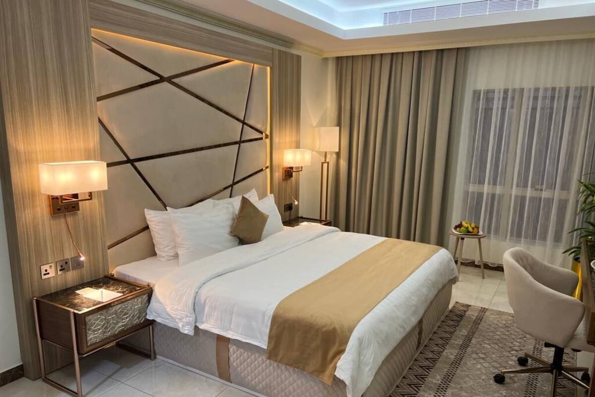 A modern hotel room with a large bed, two bedside lamps, a nightstand, a chair, and a small table with fruit.