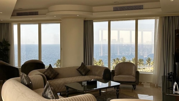 A spacious living room with a large sofa, armchairs, and a coffee table. The room has large windows offering a view of the ocean and a city skyline. - Seafront Luxury Suites Jeddah Corniche (Jeddah)