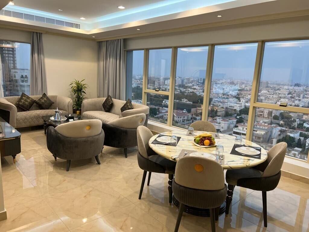 A modern living room with a dining area, large windows with a city view, and a plant.
