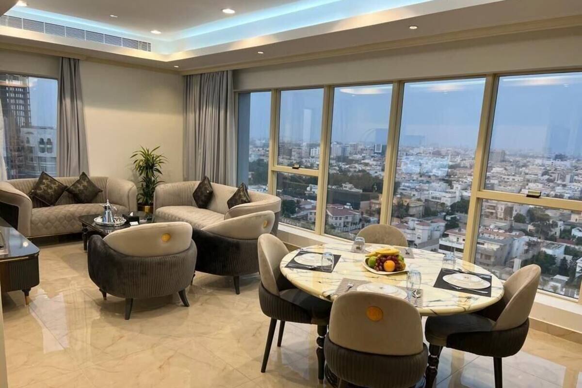 A modern living room with a dining area, large windows with a city view, and a plant.
