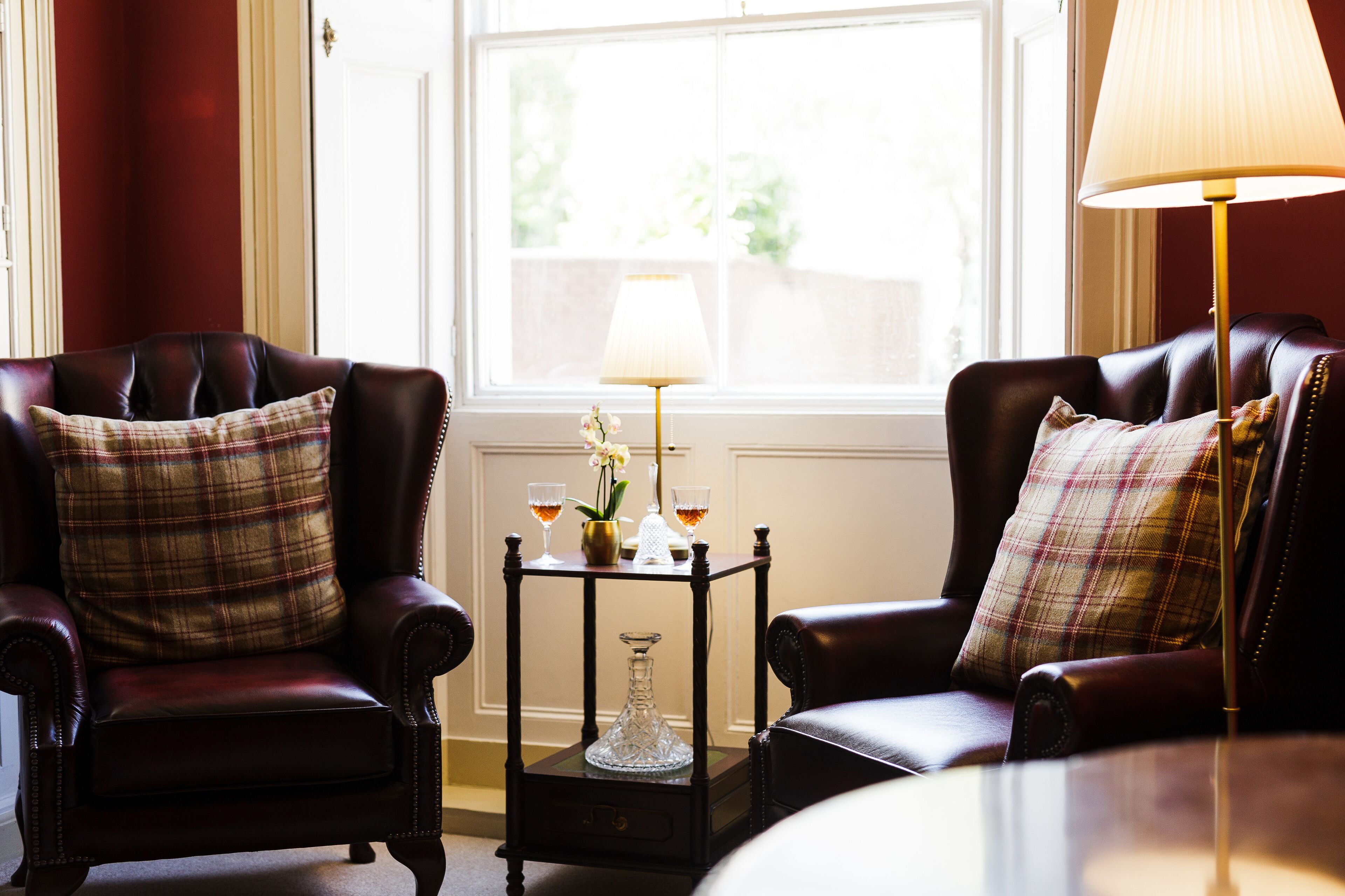 Une pièce comprenant deux fauteuils en cuir, une petite table avec une lampe et une fenêtre donnant sur un paysage verdoyant.
