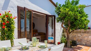 A dining area with a table set for four, surrounded by white chairs, and a view of the interior through a glass door. - Cubo's Finca La Graciosa / private pool / free wifi (Alhaurin de la Torre)