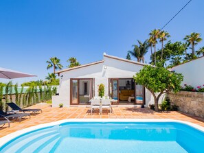 Ein Haus mit Schwimmbad, Terrasse mit Stühlen und einem kleinen Garten.