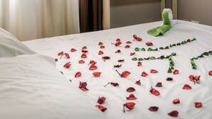 A hotel room with a bed, a nightstand, a wall-mounted light, and a potted plant.
