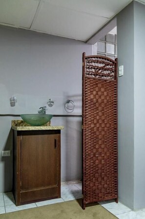 A bathroom with a wooden cabinet, a green glass sink, and a woven privacy screen. - Del Cafetal CR (San José)