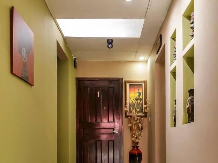 A hallway with a wooden door, a framed painting, and a vase on the wall.