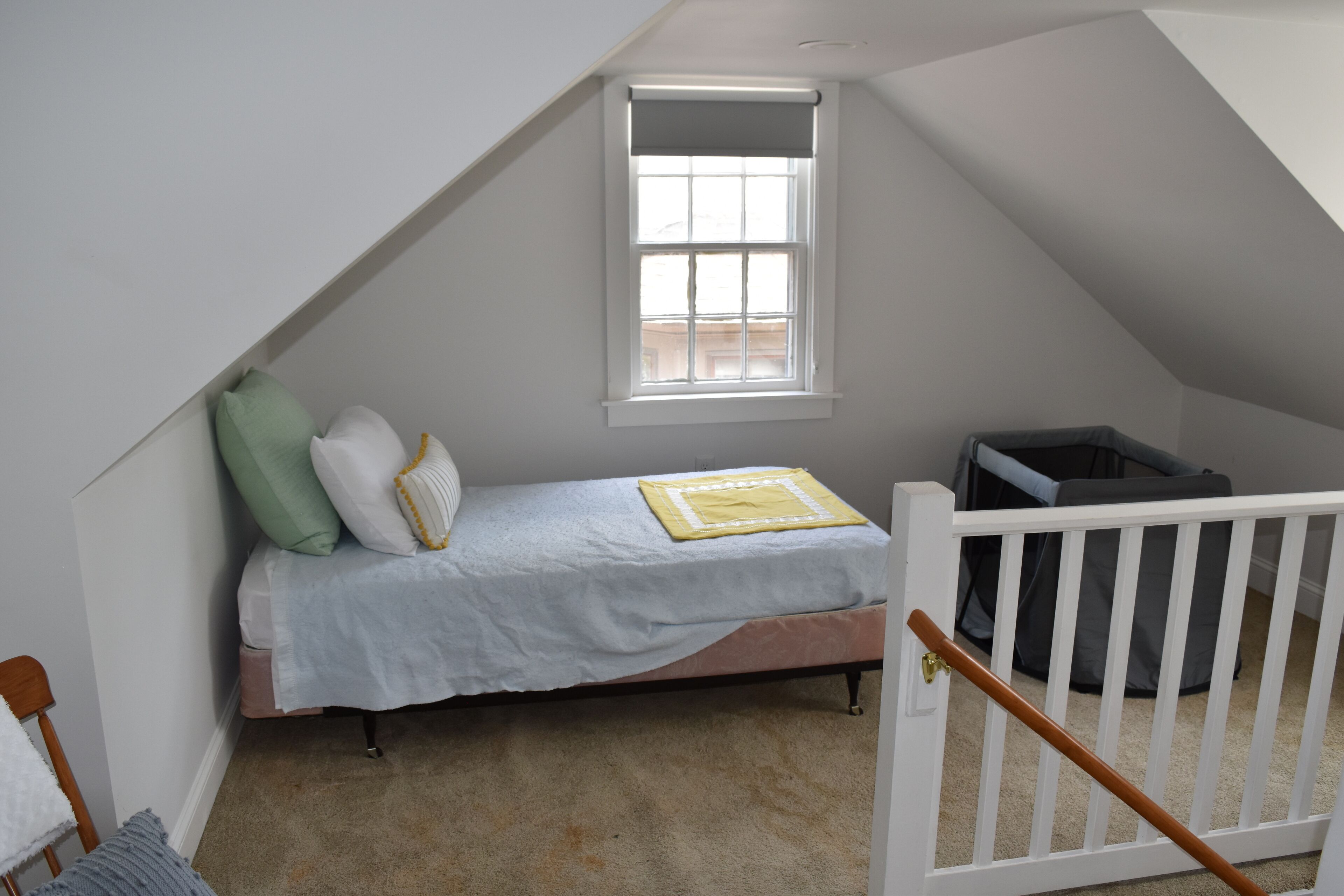 A small, single-bed room with a sloped ceiling, a window, and a white crib.