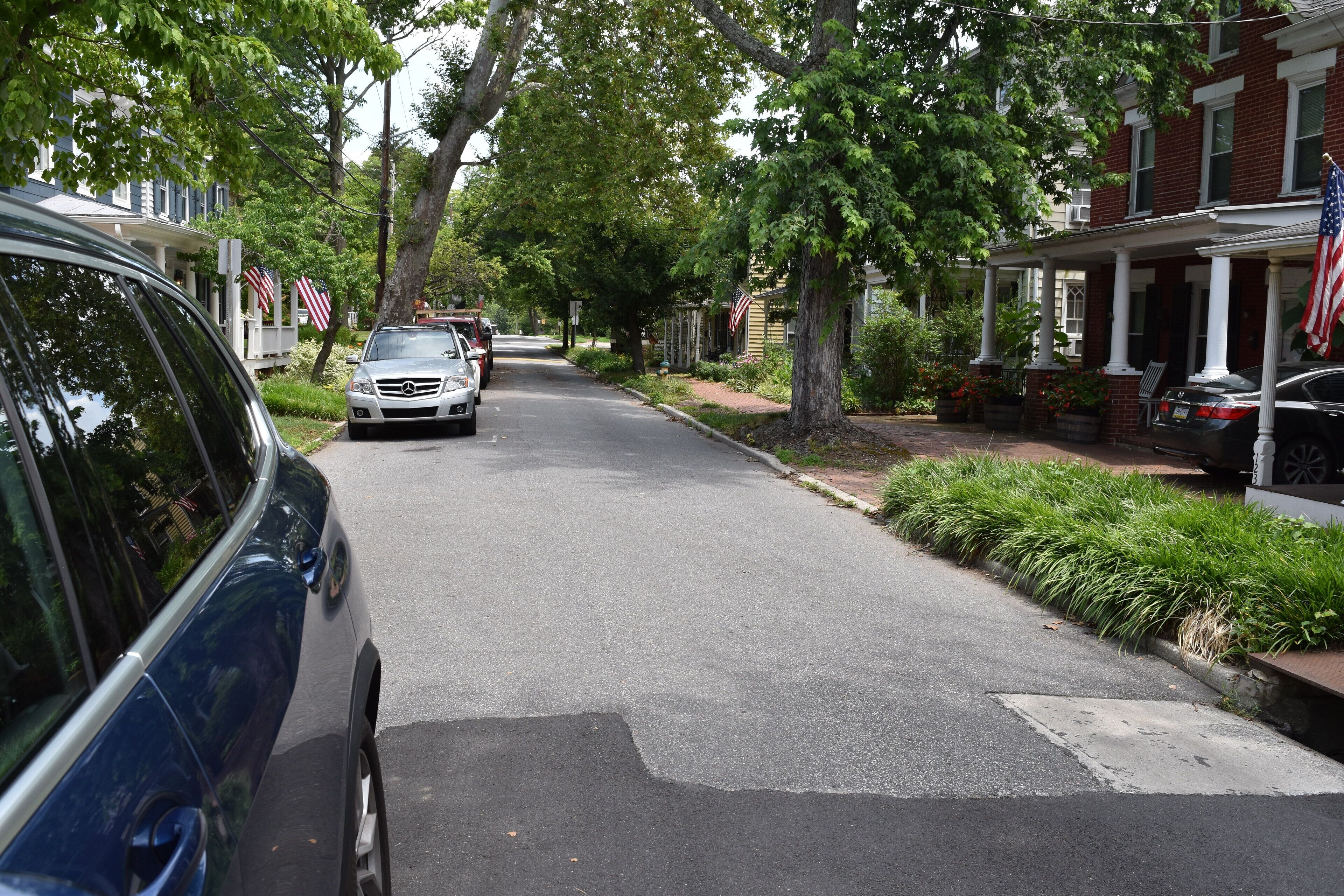 A residential street with houses, parked cars, and American flags.