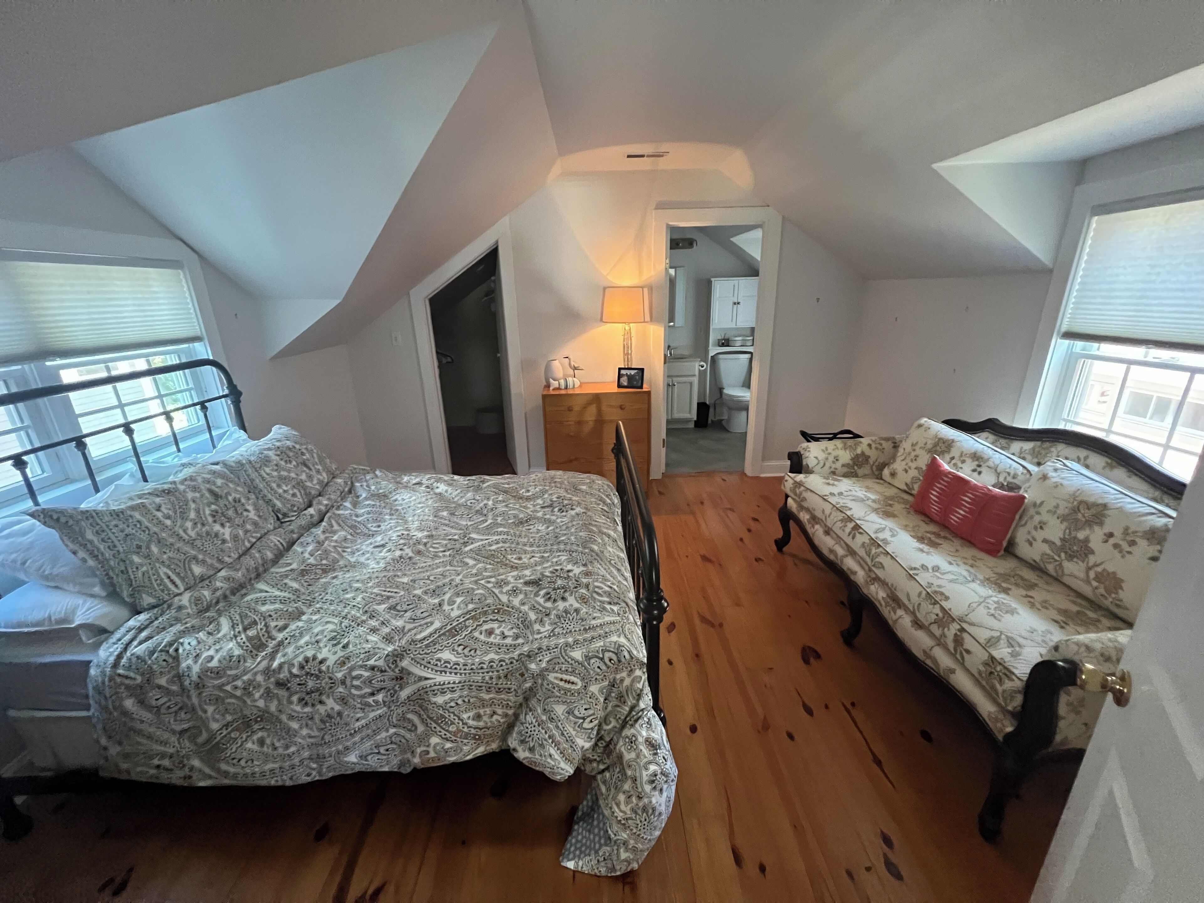 Un dormitorio con cama, suelo de madera, sofá y vistas a una cocina a través de un puerta abierta.
