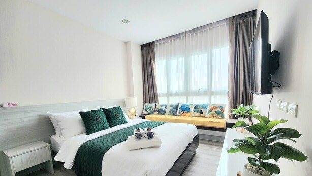 A modern hotel room with a bed, bedside table, TV, and a window with curtains. - The Prio Condo (Chiang Mai)