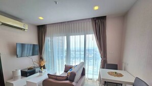 A modern living room with a sofa, a dining table, and a TV mounted on the wall. - The Prio Condo (Chiang Mai)