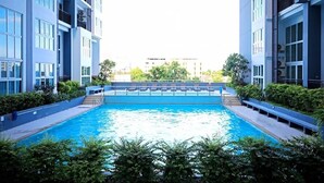 A swimming pool surrounded by modern buildings with balconies, clear skies, and greenery. - The Prio Condo (Chiang Mai)