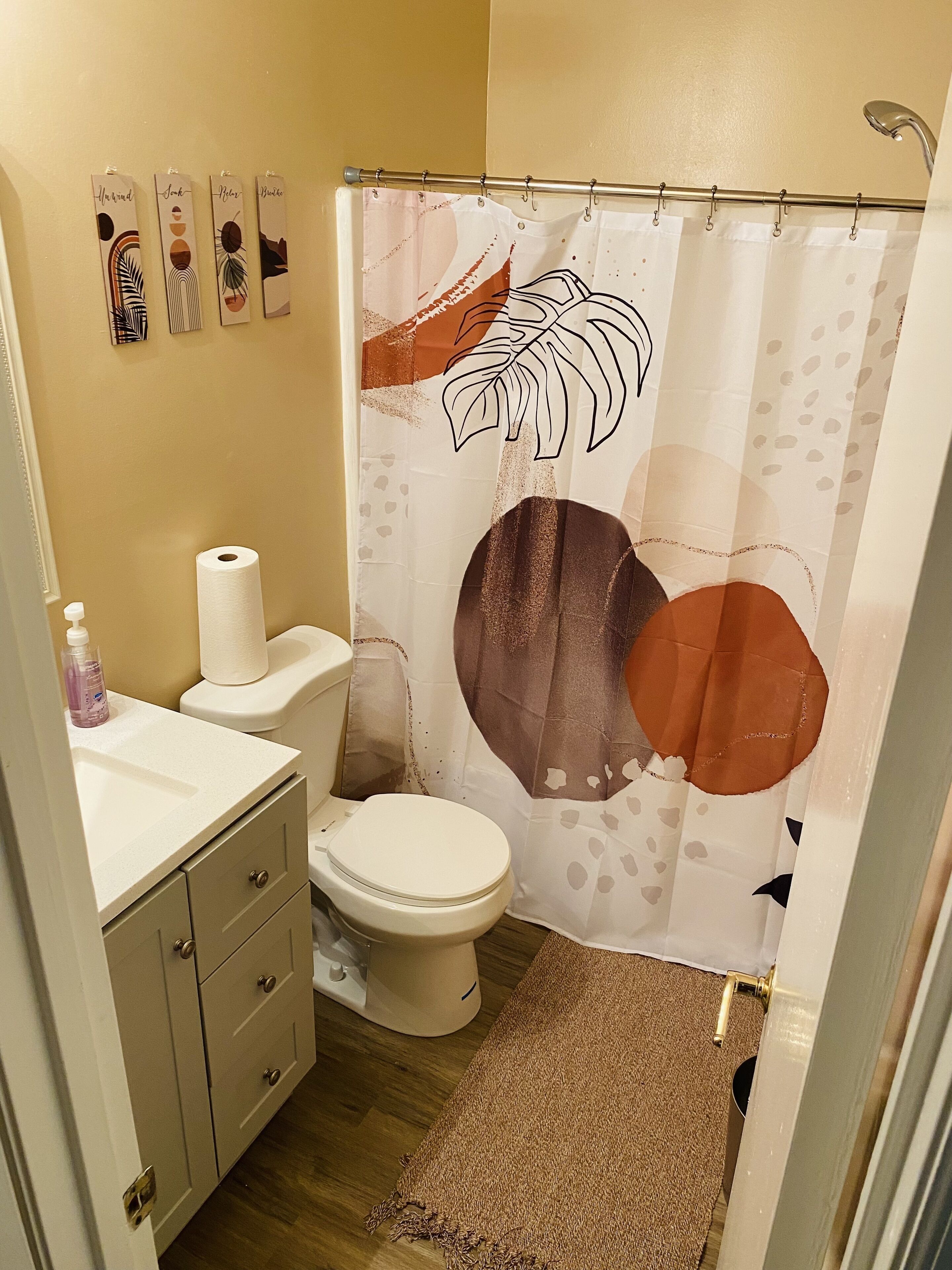 A bathroom with a toilet, a sink, a shower curtain with abstract designs, and a small rug.