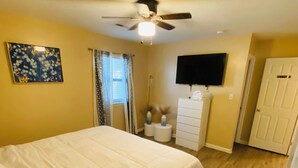 A bedroom with a bed, a ceiling fan, a TV, a dresser, and a door.