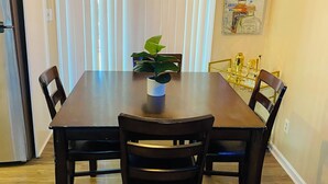 A dining area with a wooden table and chairs, a potted plant, and a hanging light fixture.