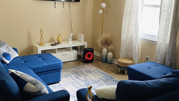 A modern living room with a flat-screen TV, blue sofas, a coffee table, and a ceiling fan.