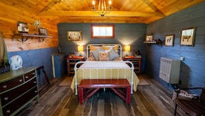 A cozy bedroom with a wooden ceiling, a bed with a bench, bedside lamps, and wall-mounted shelves with pictures. - Cozy Cabin at Farm Stay in Maine (Turner)