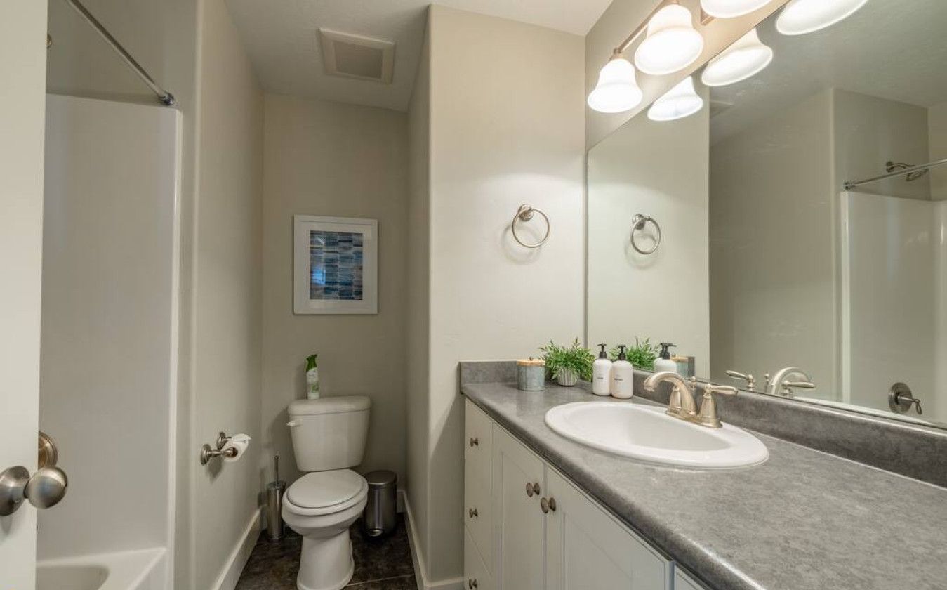 A bathroom with a white toilet, a sink with a large mirror, and a shower area.