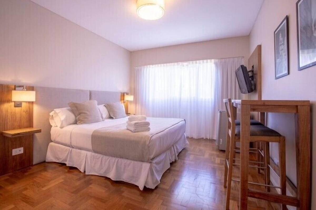 A hotel room with a large bed, a desk, and a chair.