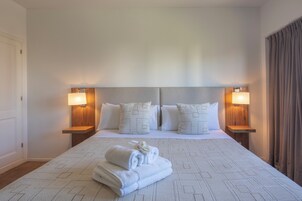 Una habitación de hotel con una cama grande, dos mesitas de noche con lámparas y una toalla doblada con cuidado sobre la cama.