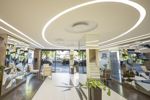 Un interior moderno con superficies reflectantes, una planta en el centro y vistas a la calle.