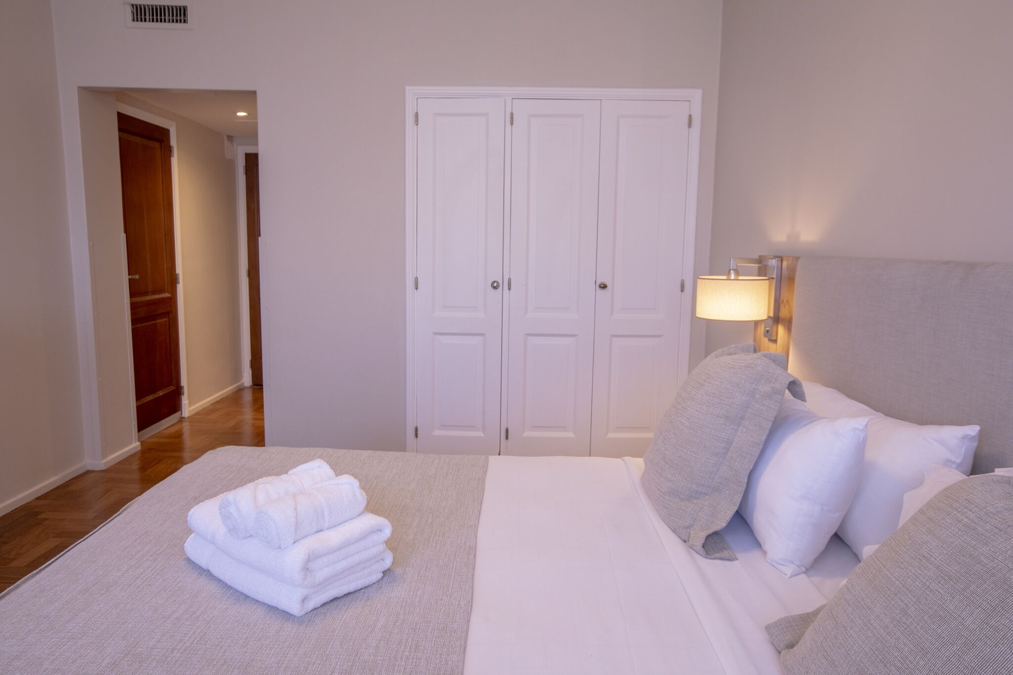 Una habitación de hotel con una cama, un juego de puertas dobles blancas, una lámpara y una pila de toallas blancas en el suelo.