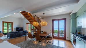 A spacious living area with a dining table, sofa, and a staircase leading to a balcony.