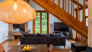 A modern living room with a wooden staircase, a fireplace, and a large TV.