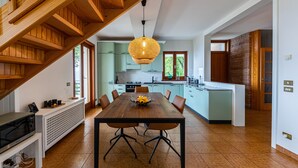 A modern kitchen with a wooden staircase, a dining table with chairs, and a hanging light fixture.