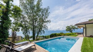 A swimming pool with wooden deck and lounge chairs, surrounded by greenery and a view of distant mountains.