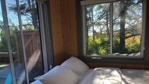 A bedroom with a bed, a window, and a view of trees and a wooden deck outside.