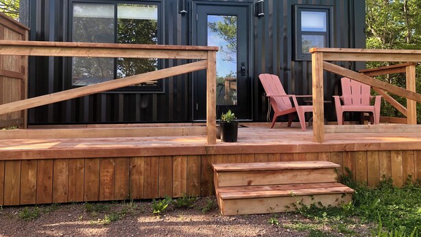 A modern, compact cabin with a deck, two windows, and a door.