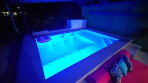 A hot tub with a blue light, surrounded by a red couch and a stone wall.