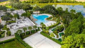 Vista aérea de un resort con una gran piscina, canchas de tenis y exuberante vegetación.