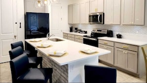 Una cocina moderna con armarios blancos, una isla central e iluminación colgante.