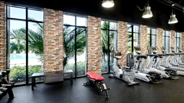 Un gimnasio con equipo de ejercicio, ventanas amplias y una pared de ladrillo.