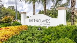 Señal que indica "The Enclaves at Festival", con un exuberante jardín y palmeras al fondo.