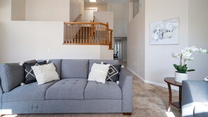 Un salon avec un canapé gris, un escalier en bois et un tableau abstrait encadré accroché au mur.