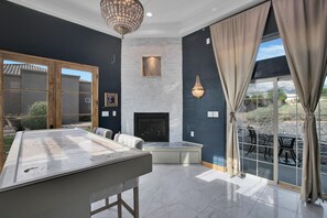 Una habitación amplia con mesa de billar, chimenea y ventanas grandes con cortinas.